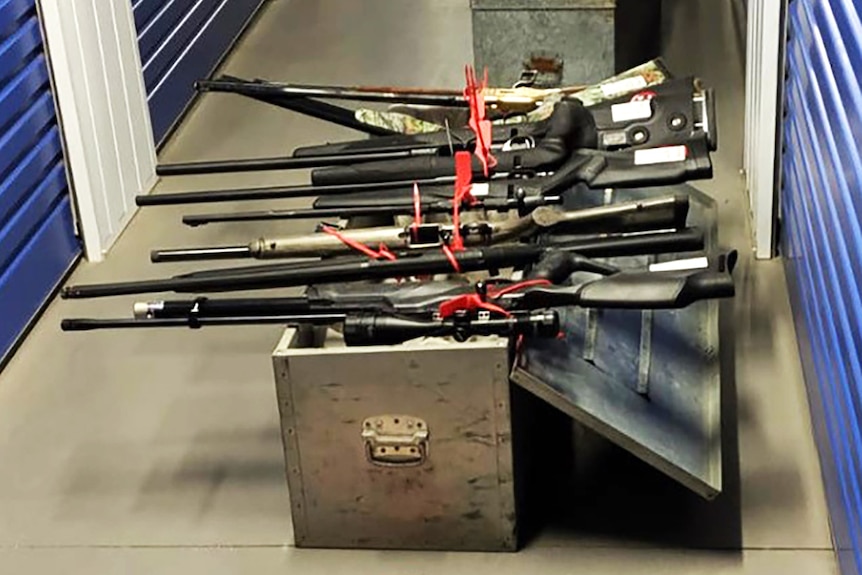 Several rifles lie on a metal cabinet in a hallway.