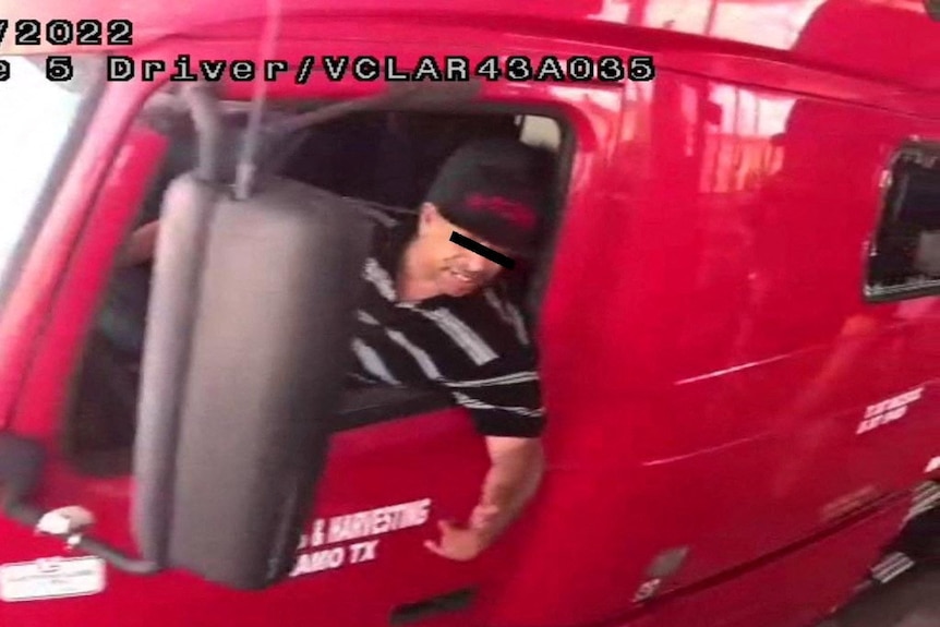 A security camera image of a man wearing a t-shirt and hat leaning out of the window of a large red truck.