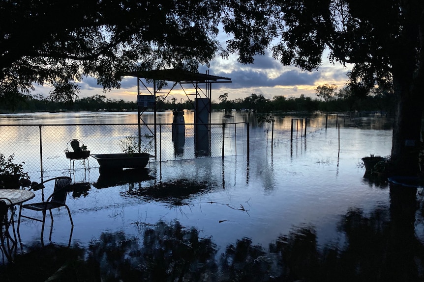 The sunset casts a blue and orange hue over the floodwaters, while underwater fuel tanks can be seen in the background