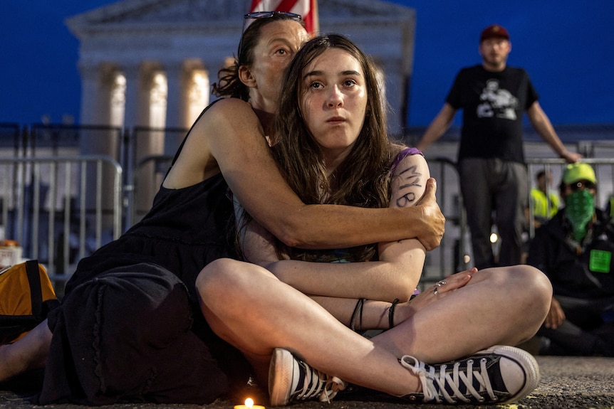 A mother hugs her teenager daughter as they sit in front on the Supreme Court at night. 