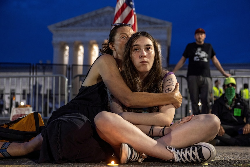 A mother hugs her teenager daughter as they sit in front on the Supreme Court at night. 
