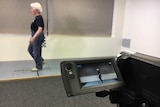 A woman walks on a plastic surface marked with lines and is filmed by small video camera on a tripod.