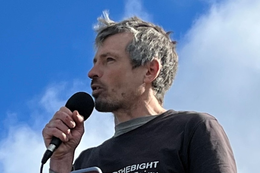 A man speaking into a microphone as he gives a speech to protestors on the beach 