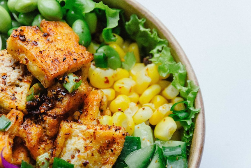 Close up of salad bowl topped with crispy flavoured tofu and spring onion.