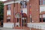 A red brick, double storey building with cream trims, arched awning, clock and flags at front