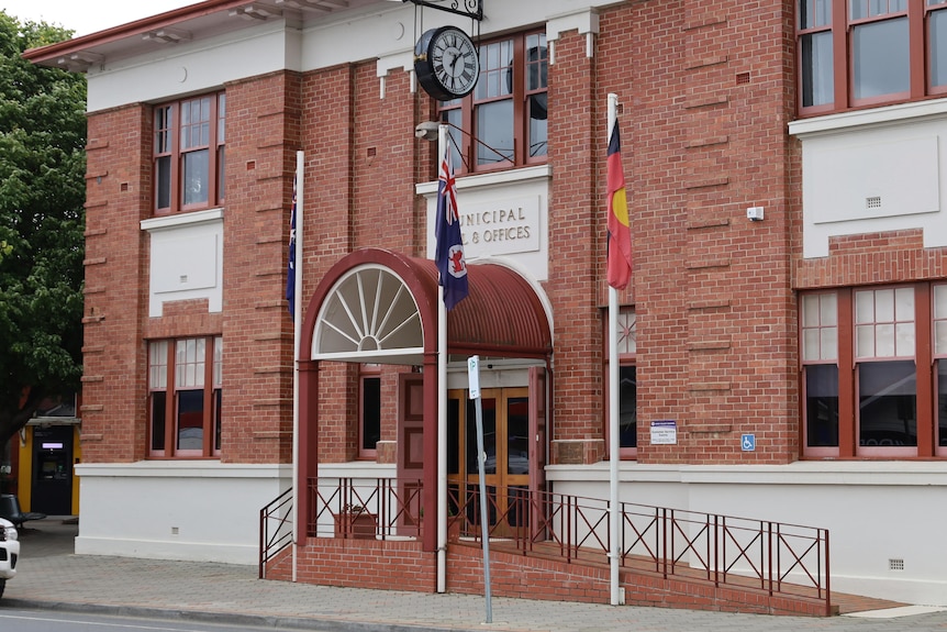 A red brick, double storey building with cream trims, arched awning, clock and flags at front