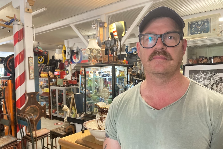 A man in glasses and a cao stands inside a shop.