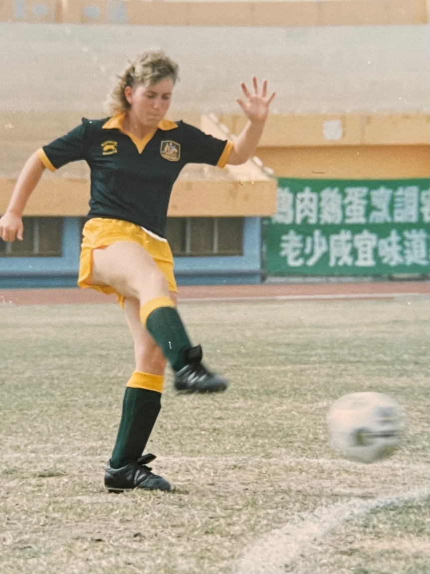 A soccer player wearing green and yellow kicks a ball during a match