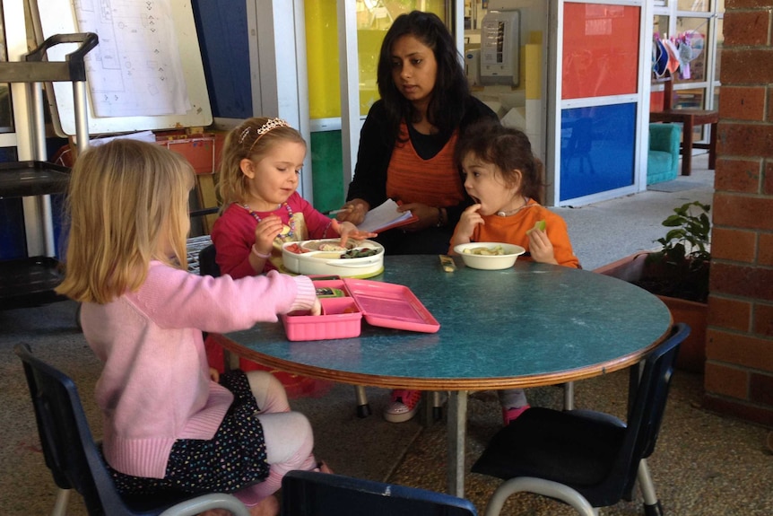 Children sit at a table eating lunch with a childcare worker at C and K childcare centre in Brisbane