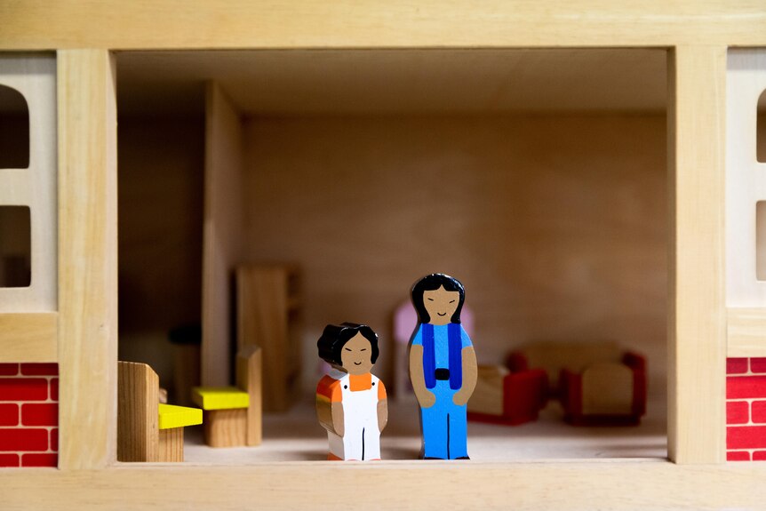 Wooden figurines of a mother and daughter in a wooden house.