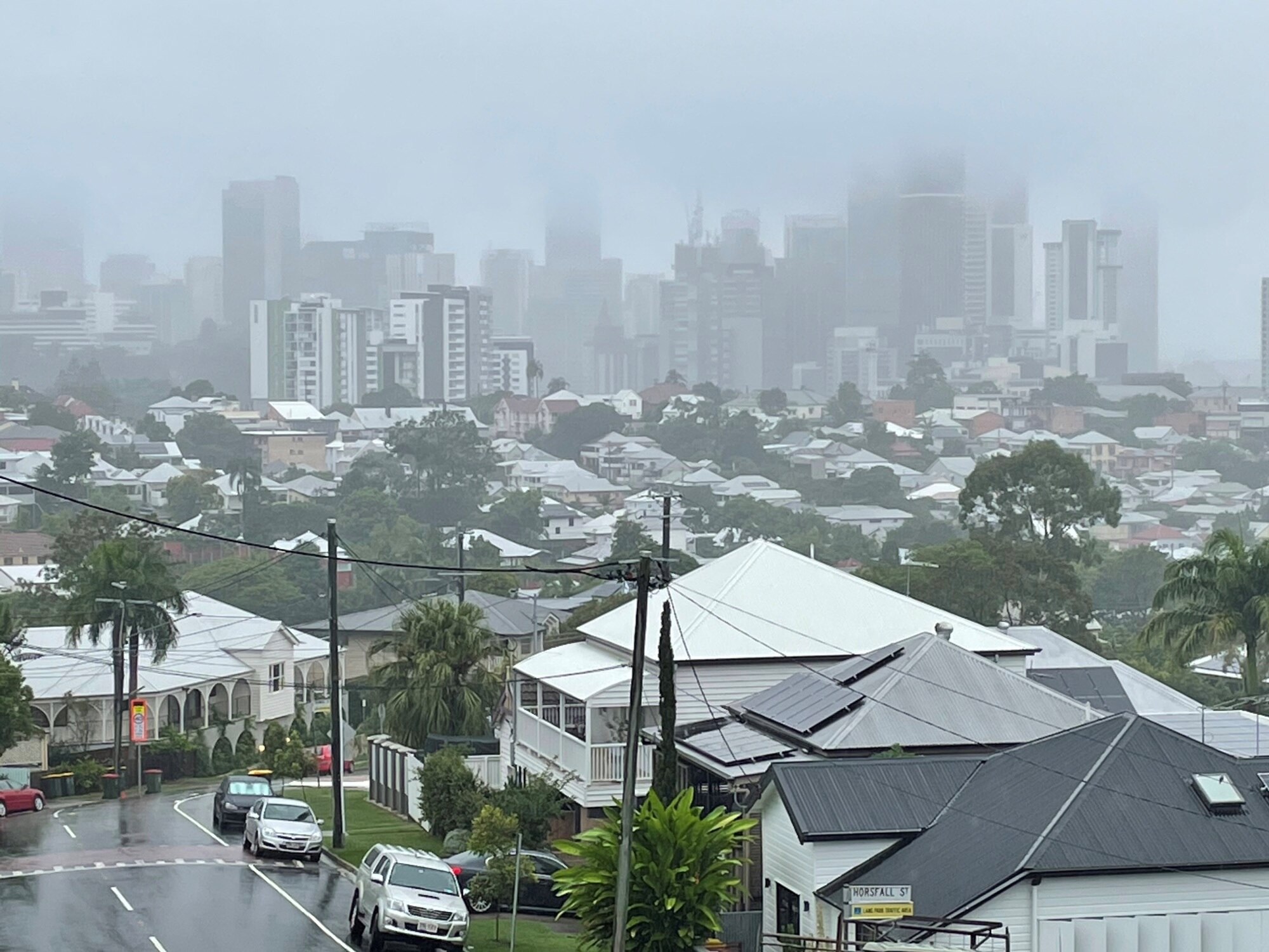 Clouds and a rain haze over the CBD in the distance behind a wet Brisbane street