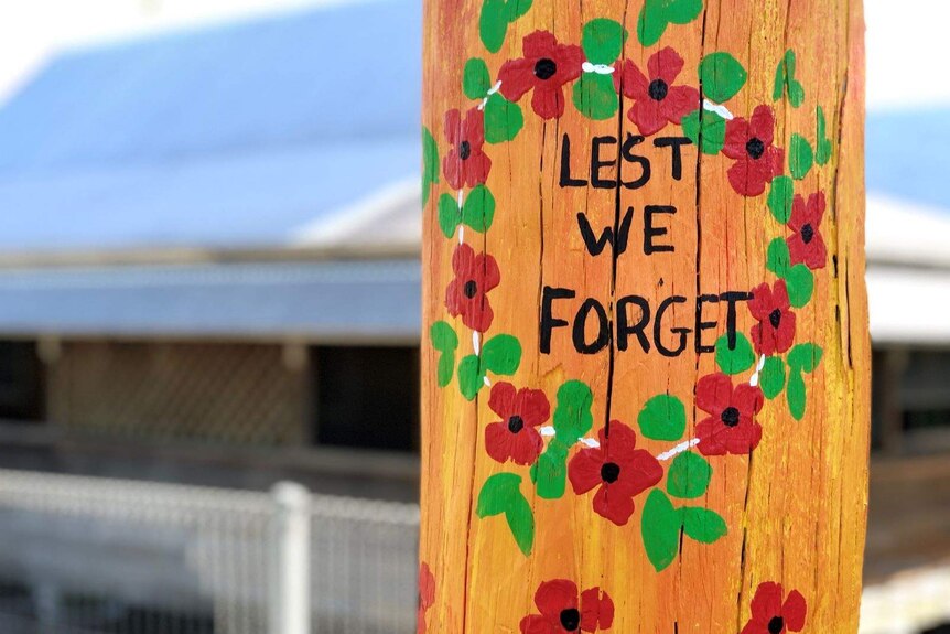 A painted wreath of poppies with the words lest we forget in the middle