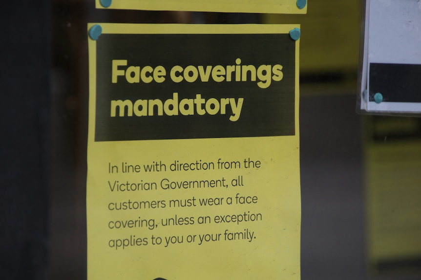 A sign saying 'face coverings mandatory' stuck to a glass window of a store.