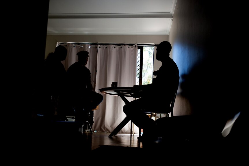 Three unidentifiable people sit in a darkened room.