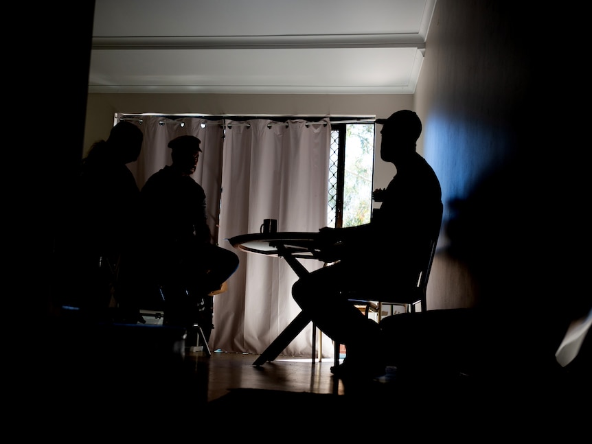 Three unidentifiable people sit in a darkened room.