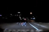 A still from dashcam video of a woman crossing the road while wheeling a bike.