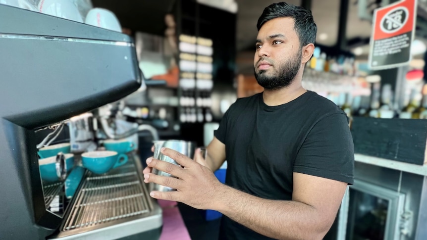一名身穿黑色 T 恤的男子在大型咖啡机上加热牛奶。