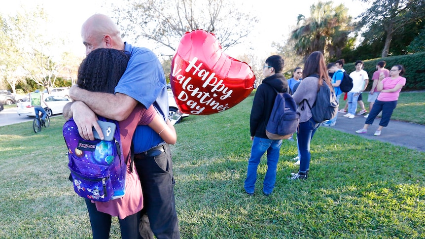 A man and a girl, who is holding a Valentines Day balloon, hug.