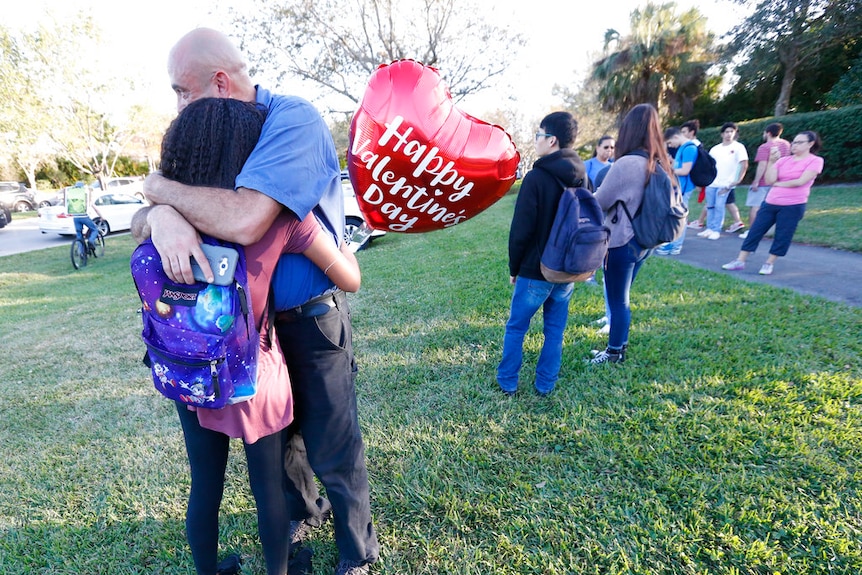 A man and a girl, who is holding a Valentines Day balloon, hug.