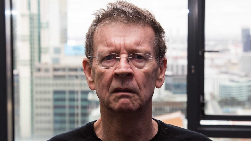 A man makes a surprised face, city in background.