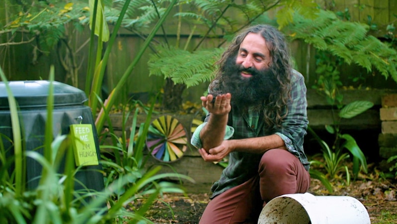 Man squatting next to compost bin looking at handful of soil