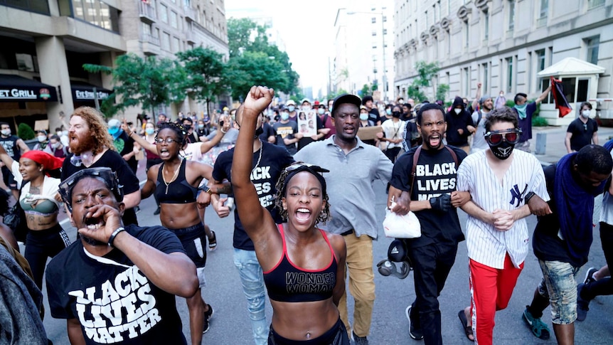 A crowd of people wearing black shirts and pants walks down a street shouting.