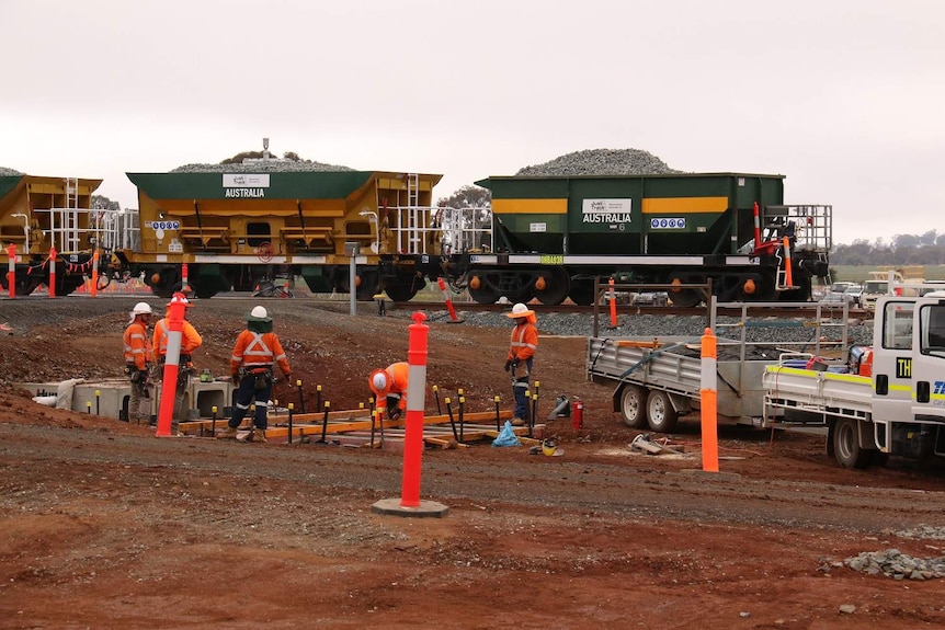 Men in high-visibility clothing work near a rail line.