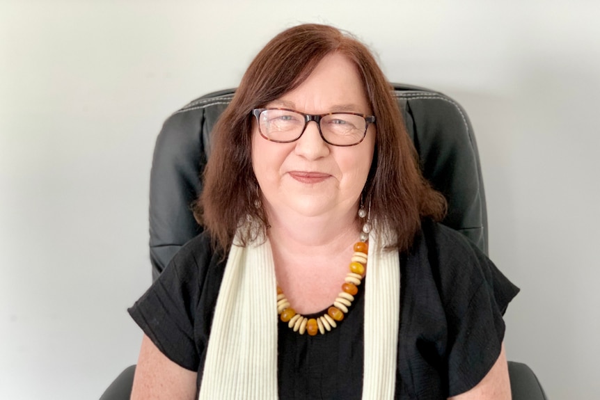 Woman sitting, smiling, in office attire.