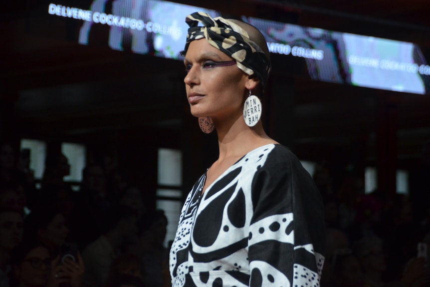 An Aboriginal Model is wearing white and black clothing with black painted on their face