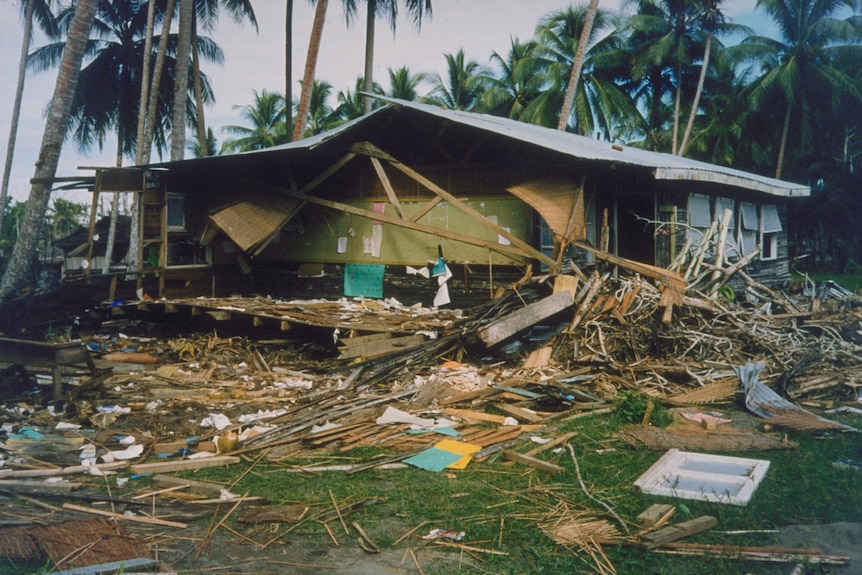 A broken school room hit by tsunami waves surrounded by debri and coconut trees. 