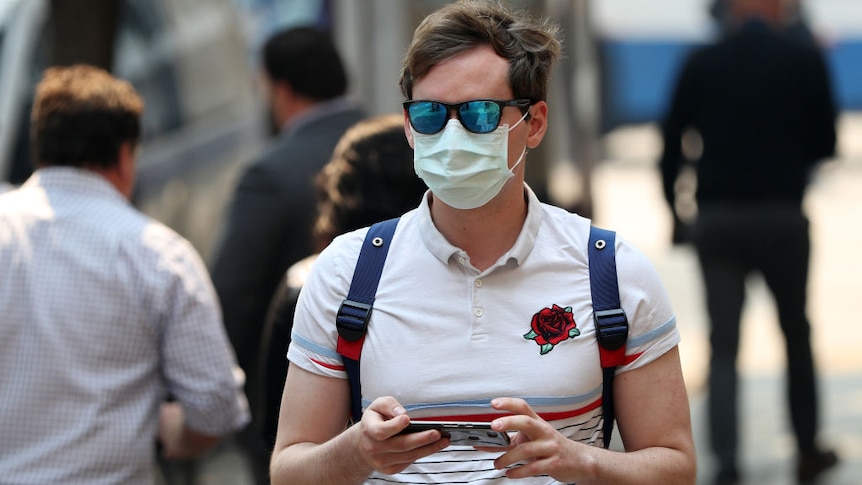 A man walks down the street with a surgeon's mask over his face.