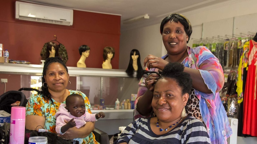 South Sudanese hairdresser, Khadija Abdalla, puts  corn rows in the hair of Margaret Jack from Papua New Guinea at Orange NSW