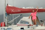 A female sailor in a pink shirt waving on board a small yacht. 