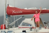 A female sailor in a pink shirt waving on board a small yacht. 