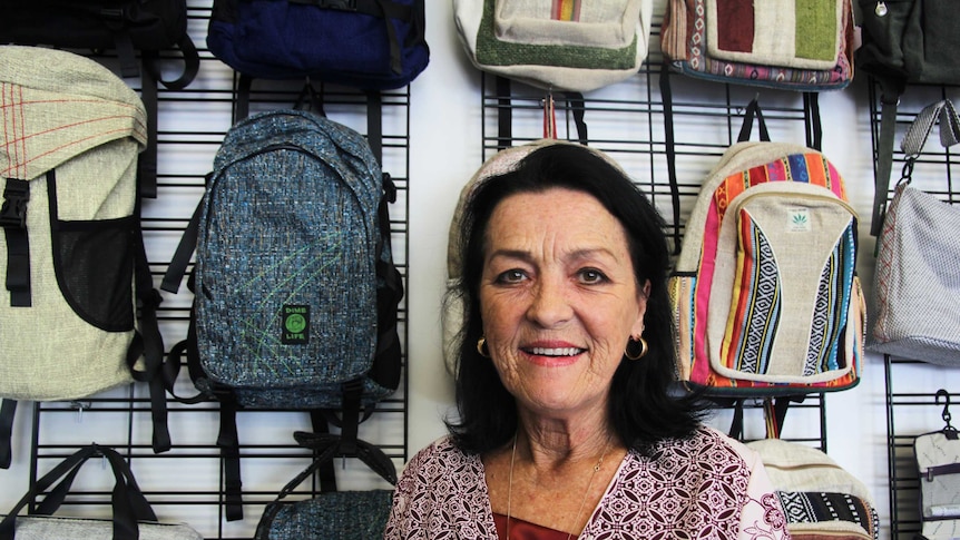 A woman smiles at the camera in front of colourful backpacks.