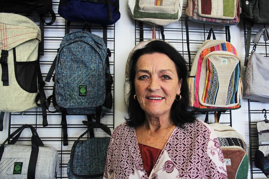 A woman smiles at the camera in front of colourful backpacks.