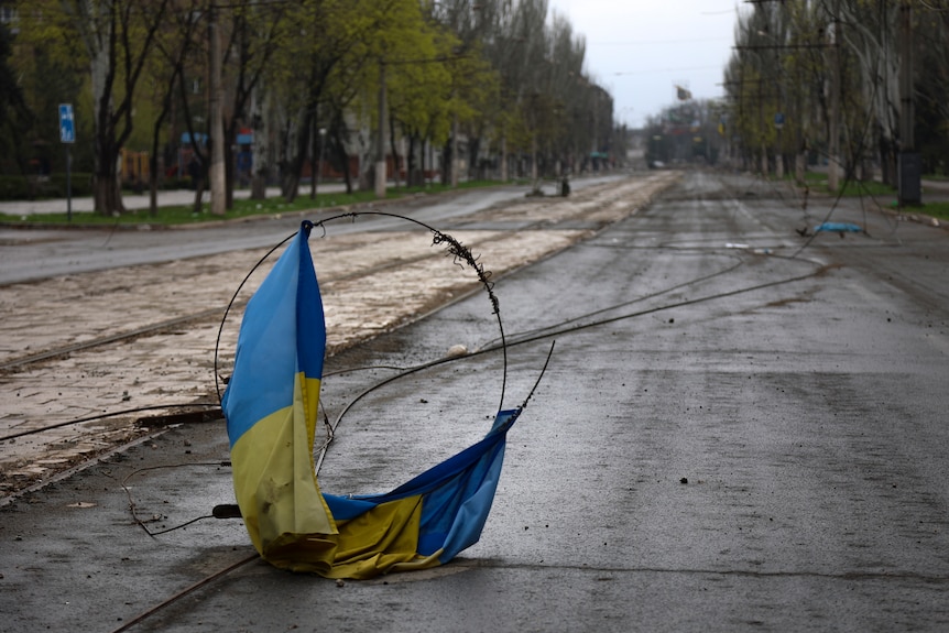 A Ukrainian flag lies wrapped in wire on the ground