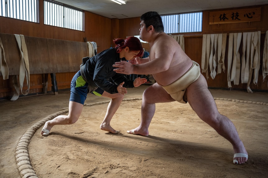 A young woman and a man wrestle in a sumo ring