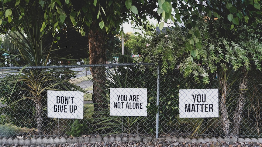 Signs on a fence that say, "Don't give up", "you are not alone" and "you matter"