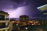 Lightning strike from dark, cloudy skies, over a city skyline.