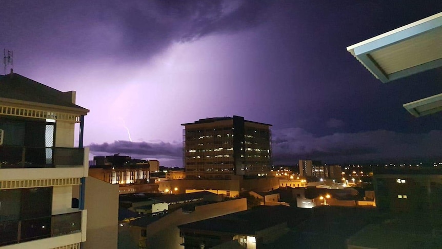 Lightning strike from dark, cloudy skies, over a city skyline.