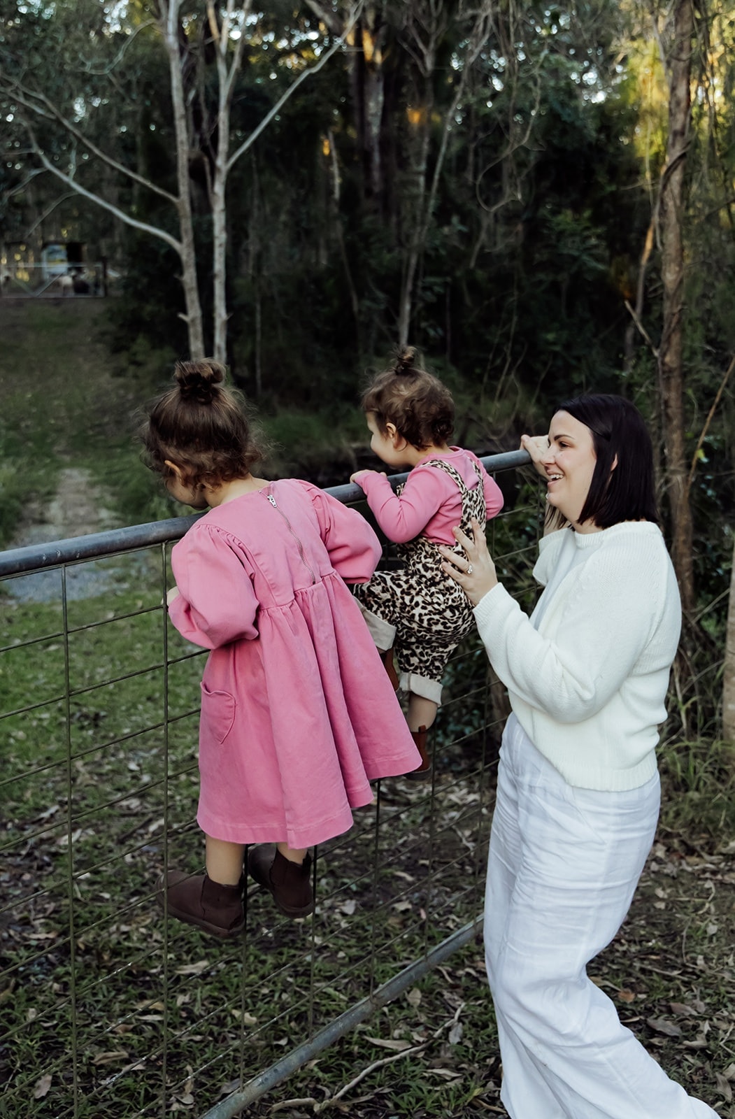 A smiling woman with two children in a rural setting.