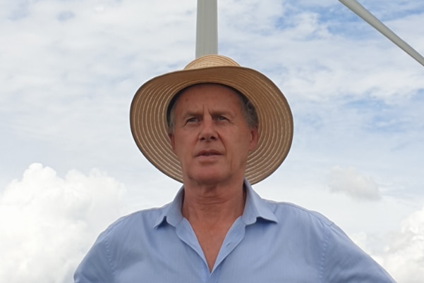A man with a straw brim hat stands in front of a wind turbine