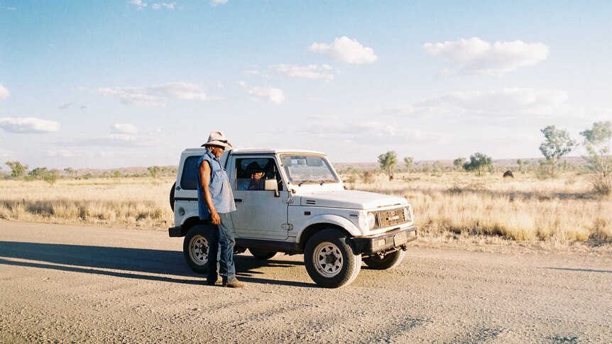 A man stands beside a car on a driveway in the Kimberleys