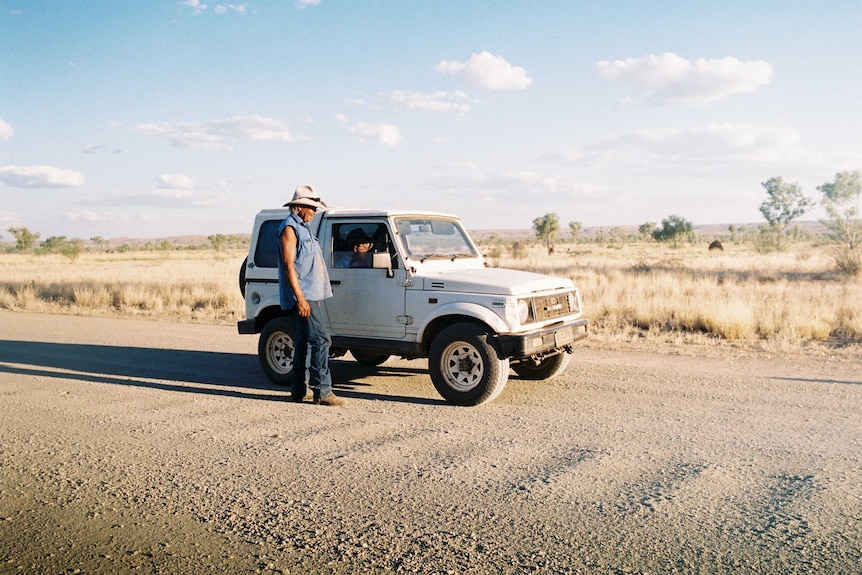 A man stands beside a car on a driveway in the Kimberleys