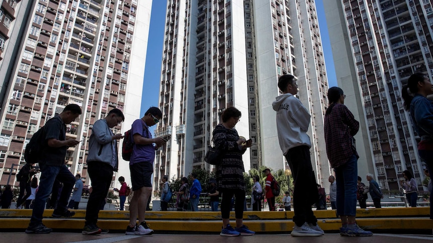 People in a line standing in front of Hong Kong skyrise apartment buildings