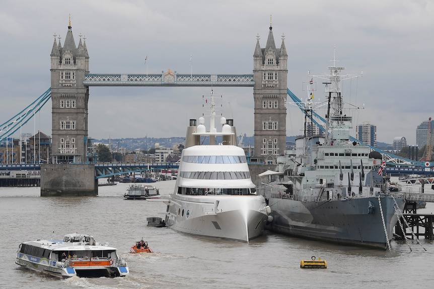 Superyacht moored beside naval ship in front of London Bridge.