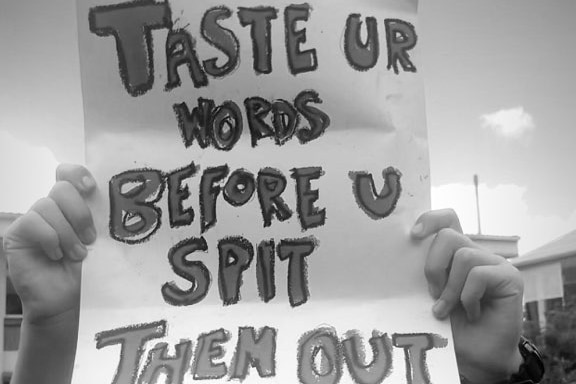 A student holds a protest banner reading 'Taste Your Words Before U Spit Them Out!'