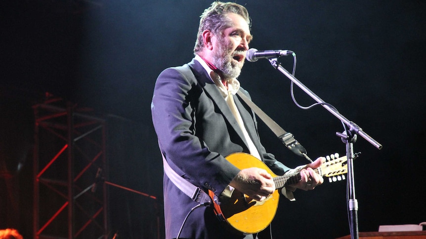 A man plays mandolin and sings on stage during a theatrical production.