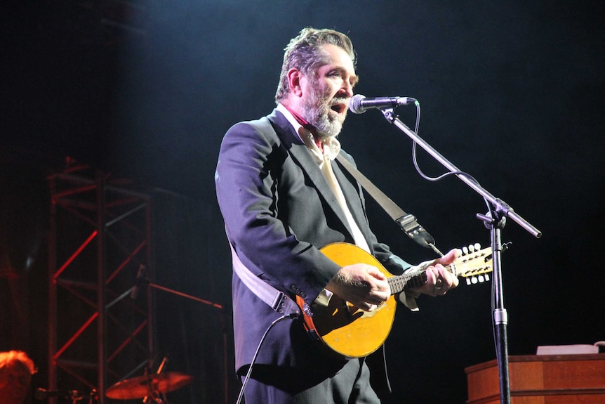 A man plays mandolin and sings on stage during a theatrical production.